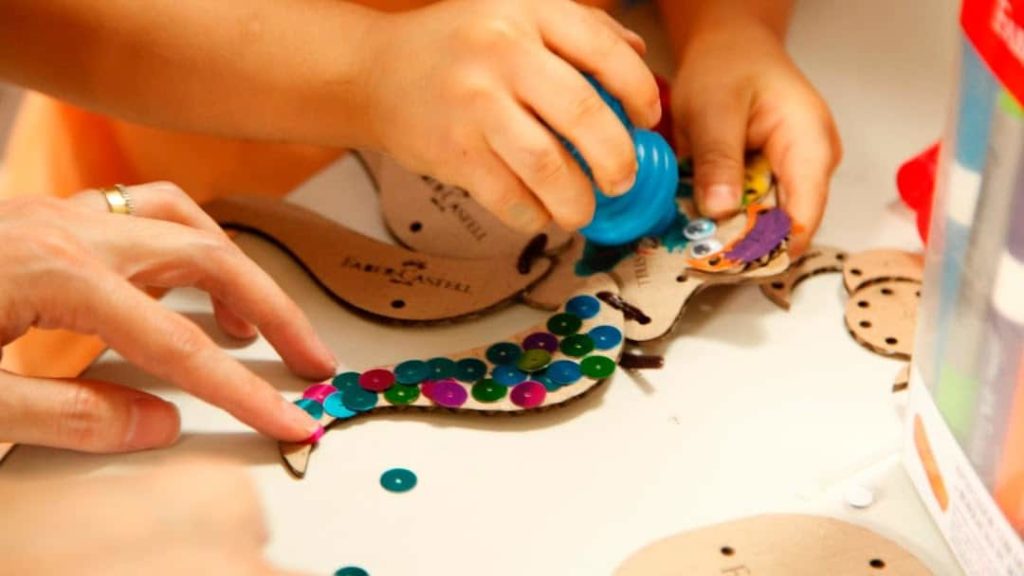 Criança realizando um projeto com tinta, lantejoulas e madeira